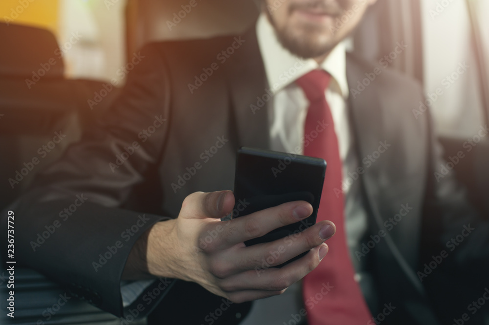 Close-up - young successful businessman sitting in the car. Handsome man manager working using his smartphone. Close-up - young successful businessman sitting in the car. Handsome man manager working using his smartphone.
