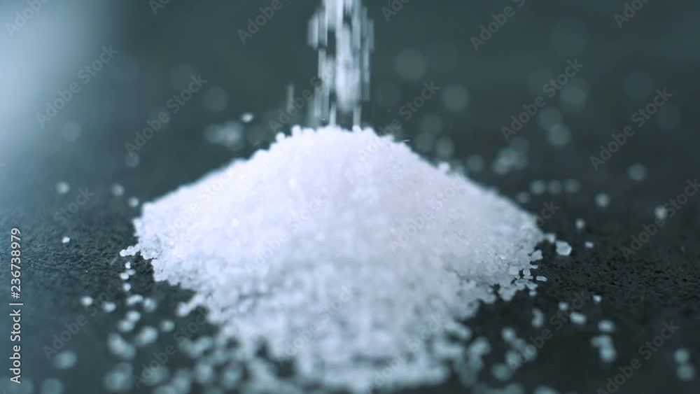 Salt falling down on dark cooking surface in slow motion. Close up.