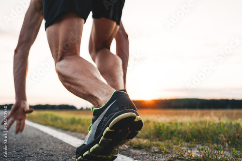 Close up view on strong and muscular athlete runner feet in start pose on asphalt road outdoor. Blurred background