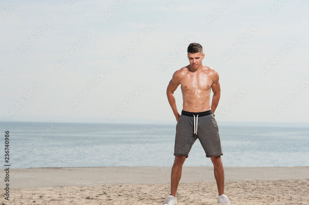 Young strong man training with kettle bell. Muscular male athlete exercising outdoors at the beach against sky. Young strong man training with kettle bell. Muscular male athlete exercising outdoors at the beach against sky.