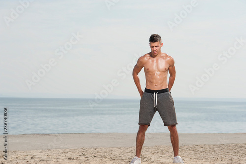 Young strong man training with kettle bell. Muscular male athlete exercising outdoors at the beach against sky.