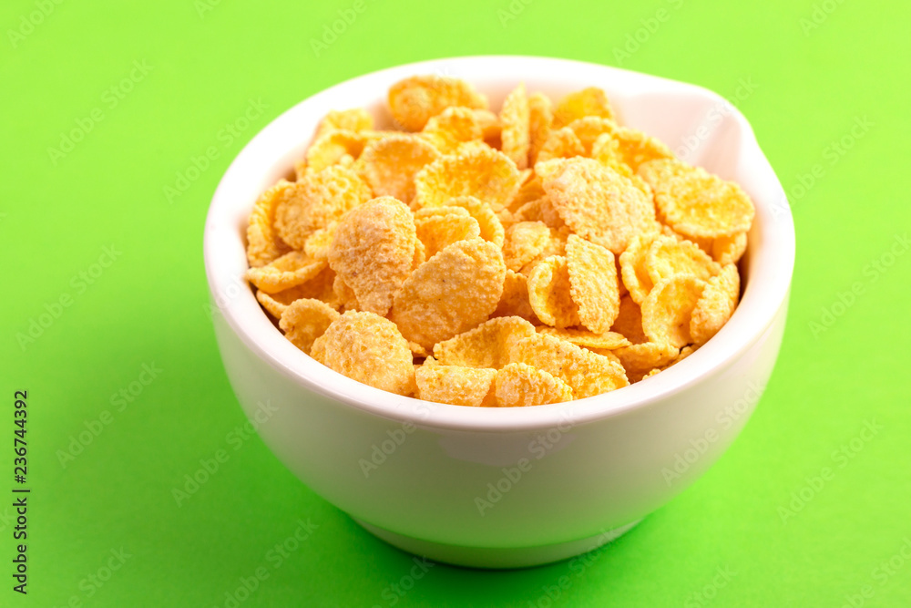 Crispy corn flakes in clay bowl on bright green background Crispy corn flakes in clay bowl on bright green background