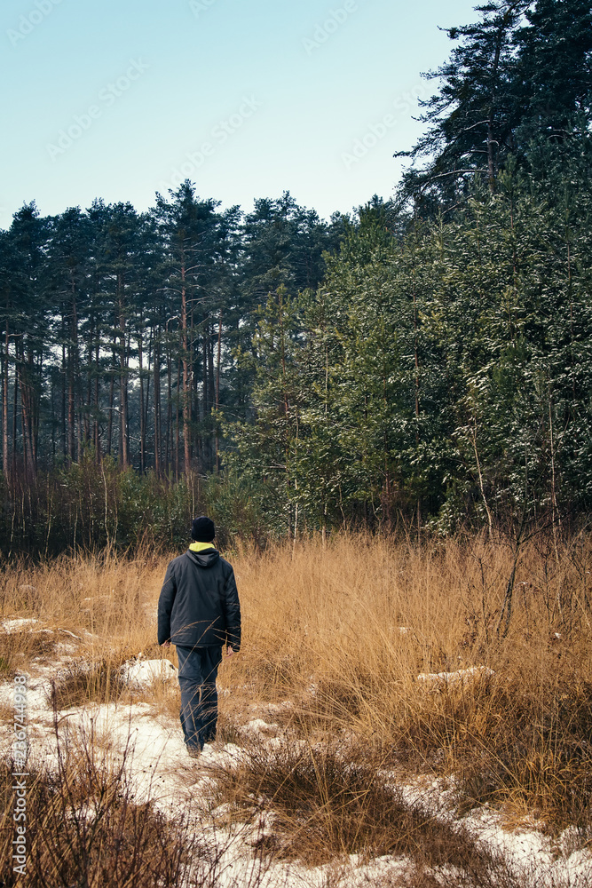 Young man walking in winter grass path with snow