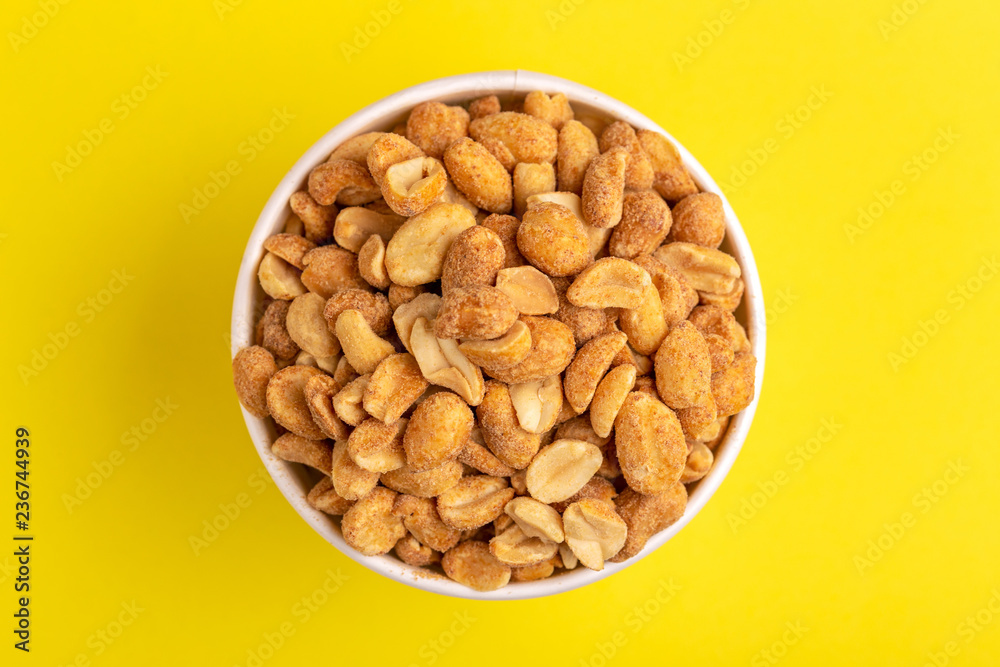Roasted peanuts in paper cup on bright yellow background.