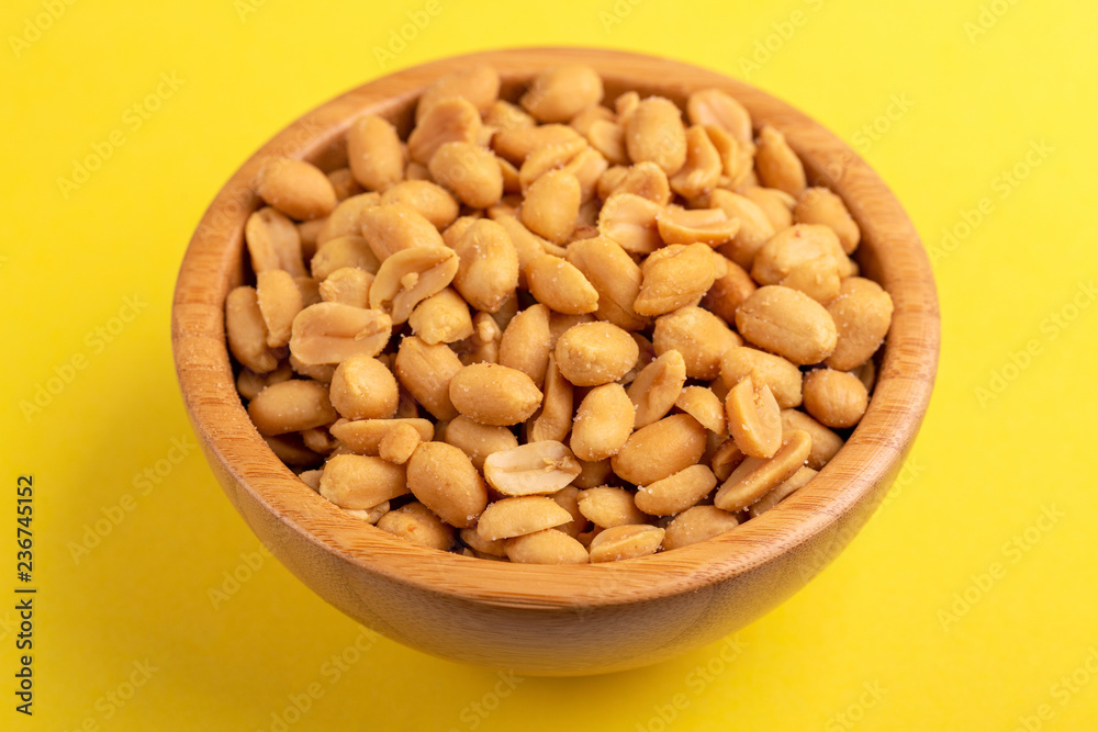 Roasted peanuts in wooden bowl on bright yellow background Roasted peanuts in wooden bowl on bright yellow background