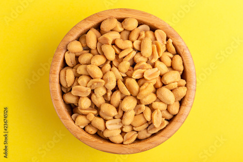 Roasted peanuts in wooden bowl on bright yellow background