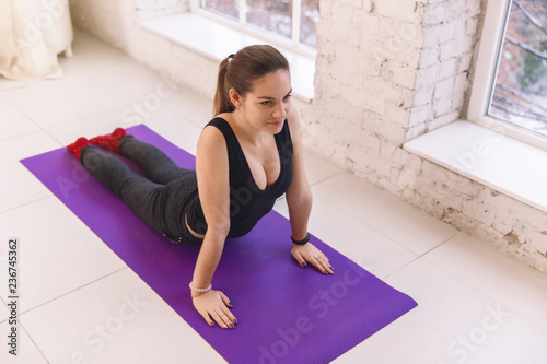 Beautiful young woman doing yoga in the pose of Urdhva mukha shvanasana in the yoga hall on the  floor near the window. Indoors yoga concept.