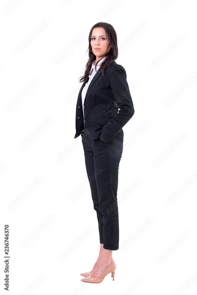 Side view of serious confident business woman looking at camera with hands in pockets. Full body isolated on white background. Side view of serious confident business woman looking at camera with hands in pockets. Full body isolated on white background.