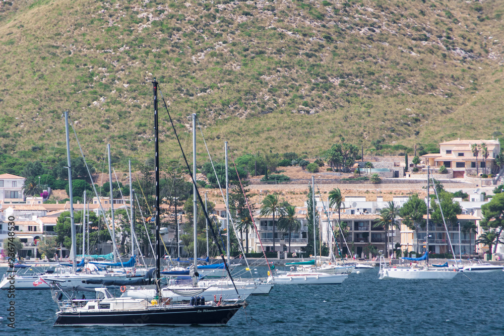 Port de Pollensa, Mallorca, Spain - July 19, 2013: View from the sea of the city, yachts, beach, streets, hotels.