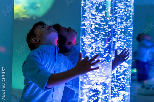 Child in therapy sensory stimulating room, snoezelen. Child interacting with colored lights bubble tube lamp during therapy session. photo