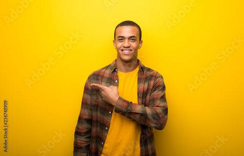 Young african american man on vibrant yellow background pointing to the side to present a product