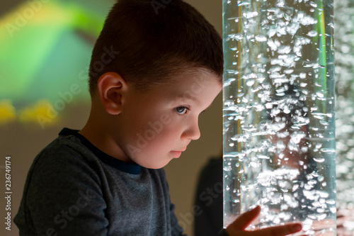 Child in therapy sensory stimulating room, snoezelen. Child interacting with colored lights bubble tube lamp during therapy session.