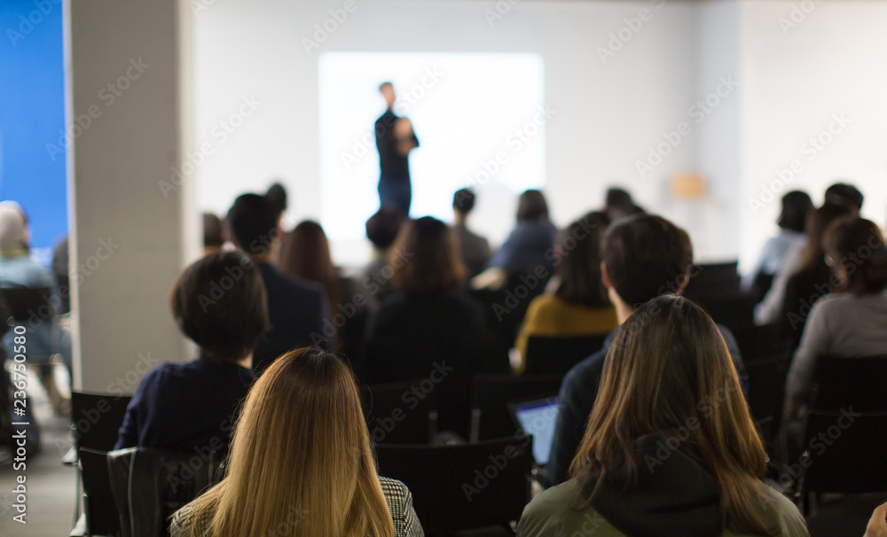 Seminar Audience in Training Room Watch Presentation. Speaker in Meeting at Business Event. Expert Presenter Giving Talk with Young Group of People. Rear View of Audience People Who Listen to Speaker.