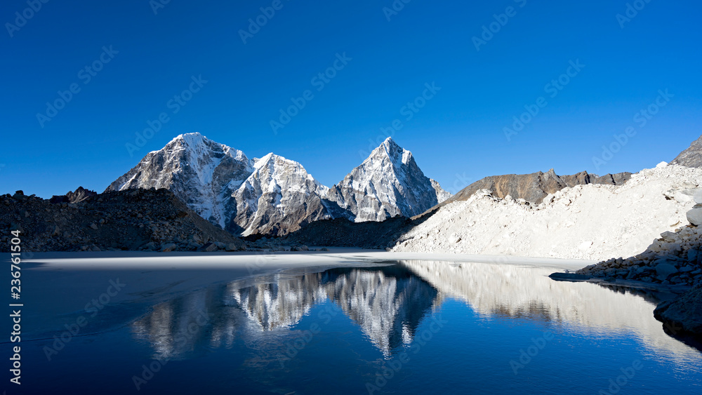 Sky and Cholatse and Tabuche mountain peaks reflect on a lake. Early morning glacier crossing along the tree passes trek before Khongma La high pass in Nepalese Himalayas.
