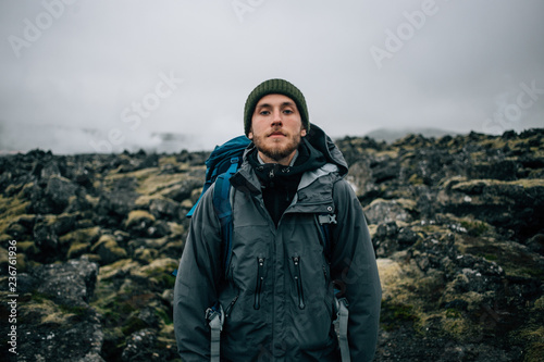Portrait of proud and brave young adventurer hiker, explorer handsome man with trekking backpack stand on rocky hiking trail or path, look into camera. Outdoor vibes and adventures wanderlust