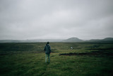 Two man, hikers or tourists walk towards clifs on rainy day in icelandic epic ladnscape or scenery. Vast open green fields and mesmerizing nature. Concept outdoor lifestyle