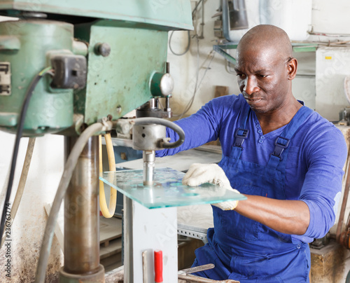 professional African American glazier working with glass on stationary drilling machine