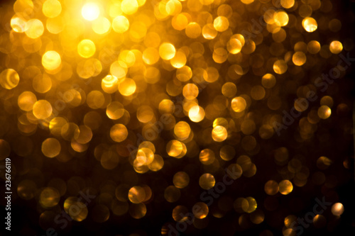 Christmas golden glowing background. Holiday abstract defocused backdrop. Tinsel blurred gold bokeh on black background