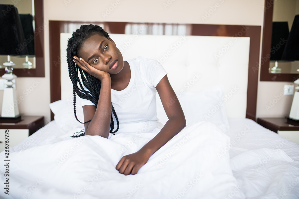 Young african Woman sitting on her bed looking bored or sleepy at the camera Young african Woman sitting on her bed looking bored or sleepy at the camera