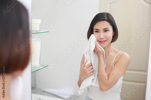 Young asian woman wiping her face with towel in bathroom.