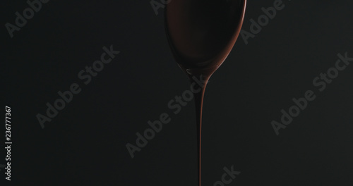 closeup melted dark chocolate dripping from spoon over black background