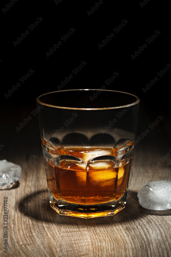 Glass of alcoholic drink with ice cubes on wooden table. Whiskey