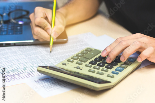 Close-up accounting man hands pressing calculator buttons and holding pencil checking documents financial report.