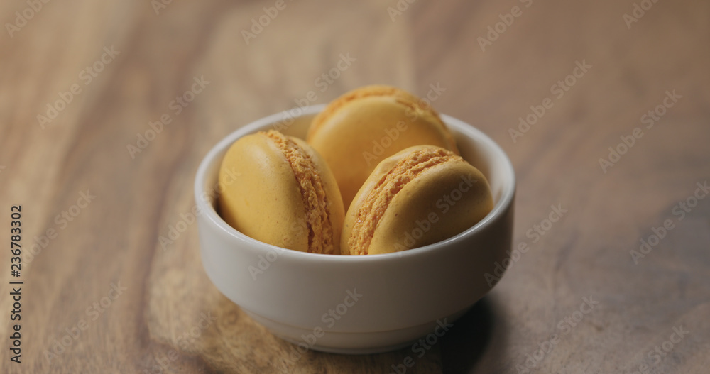 orange macarons in white bowl on wood table