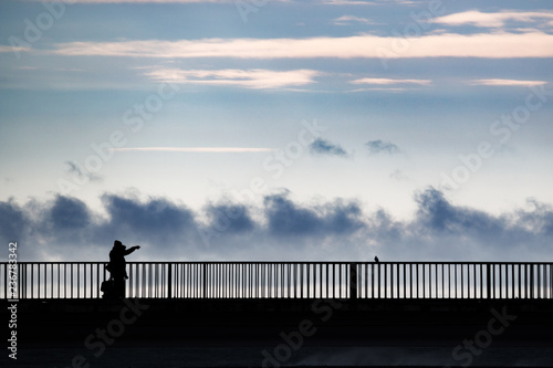 People in silhouette standing on a bridge over a sea