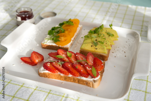Breakfast: Toast with strawberries, avocado and yellow cherry tomatoes on a plate, top view