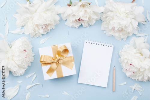 Empty notebook and gift or present box decorated white peony flowers on pastel table top view. Flat lay composition for birthday or wedding.
