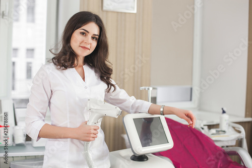 Young attractive female cosmetologist with laser epilator equipment. Doctor dermatologist holding an epilator in her hands. Cosmetology procedure with professional in beauty salon or clinic