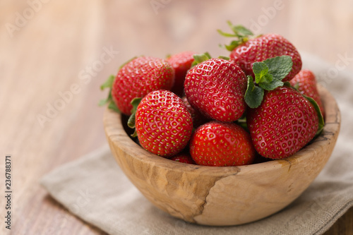 Ripe strawberries in wooden bowl on wood background with copy space