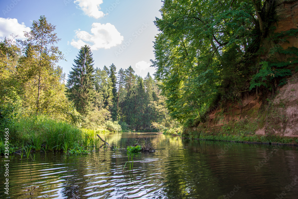 water stream in river of Amata in Latvia with sandstone cliffs, green foliage