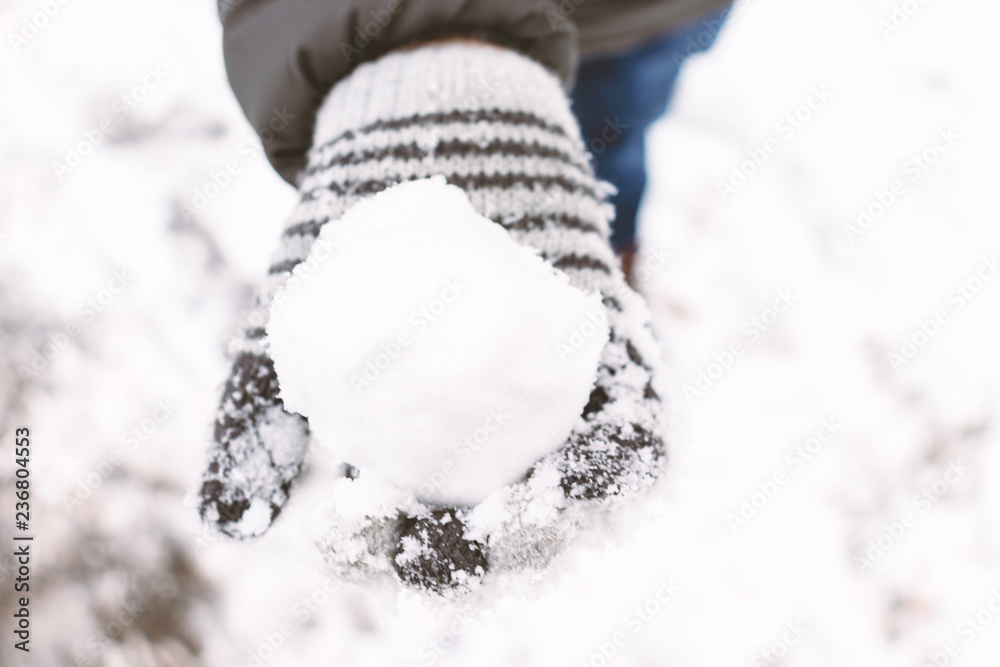A boy wearing mittens, wool gloves holding a snowball in his hand, outdoor winter activities concept