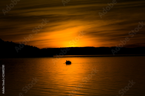 Breathtaking sunset landscape at a Chilean lake, with a boat in the middle of the orange light