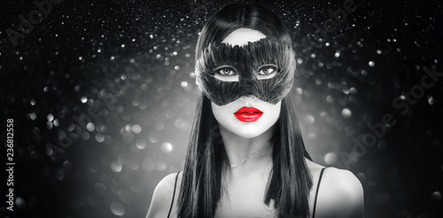 Beauty glamour brunette woman wearing carnival feather dark mask, party over holiday glowing black background
