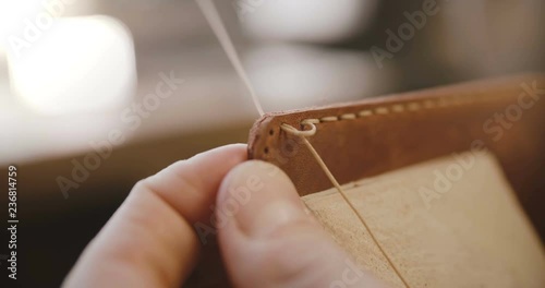 Macro close-up shot of leather sewing process details, hands with needle and strings making a bag on saddler in workshop
