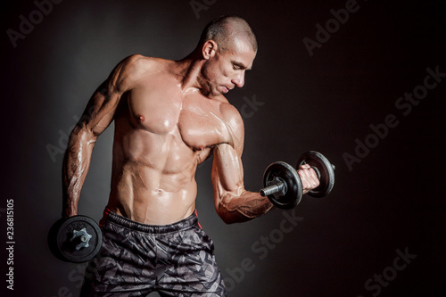A man shakes his arm muscles. Man with dumbbells. Strong man. Strength exercises. Muscle man. Pumped up muscles. Muscle mass. Dumbbell. Sport equipment.