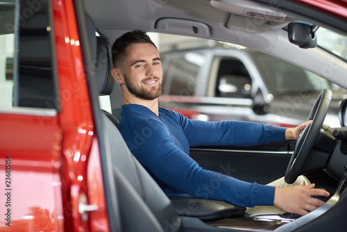 Brunette handsome man in blue sweater smiling in red car.