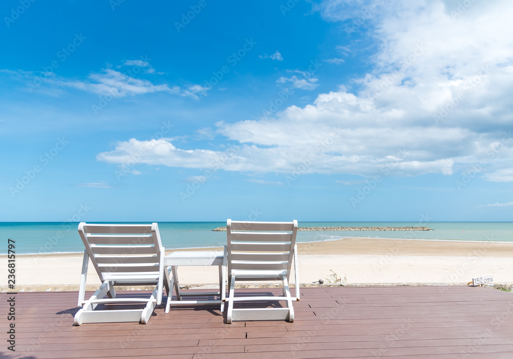 two deckchairs on jetty in front of tropical island with beautiful sand beach, beach chairs by the sea with bright sky in the summer vacation. two deckchairs on jetty in front of tropical island with beautiful sand beach, beach chairs by the sea with bright sky in the summer vacation.