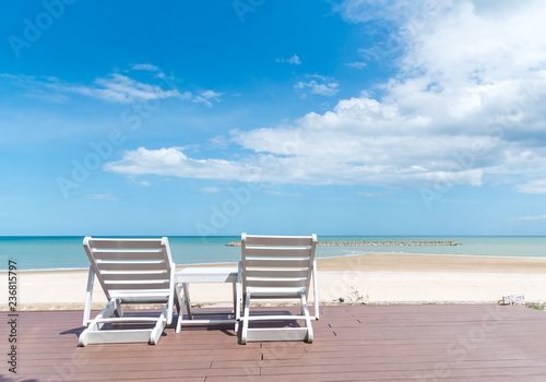 two deckchairs on jetty in front of tropical island with beautiful sand beach, beach chairs by the sea with bright sky in the summer vacation.