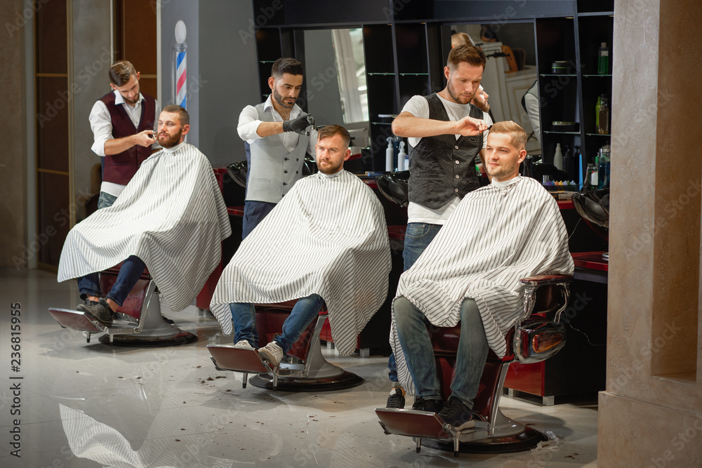 Obraz premium Three barbers doing styling of hair and beard in barber shop