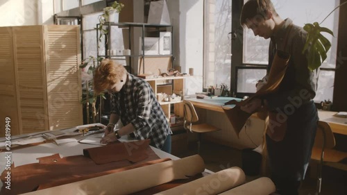 Small craftsmanship artisan business partners cooperate in handmade leather goods production process in a workshop.