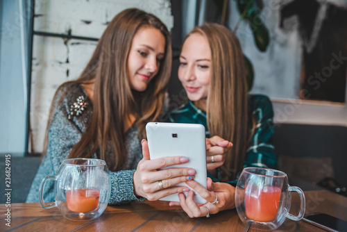 two women talking in cafe drinking tea looking tablet