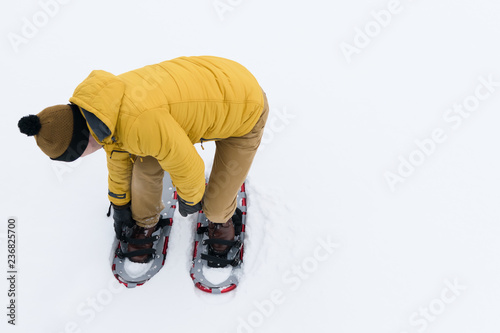 man in a yellow jacket puts snowshoes on white snow
