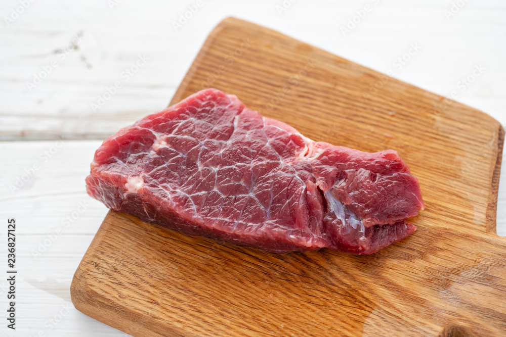 Morning in the kitchen. Raw meat. Raw fresh beef steak on a wood cutting board. White wooden background, top view, copy space, Daylight Morning in the kitchen. Raw meat. Raw fresh beef steak on a wood cutting board. White wooden background, top view, copy space, Daylight
