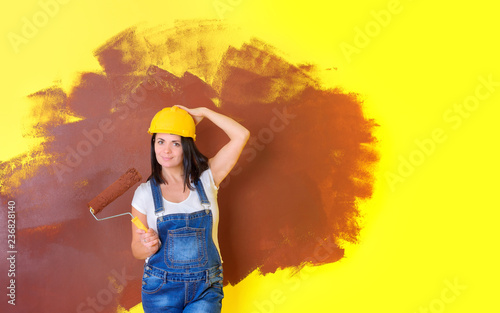 woman painter in a construction helmet with a paint roller, the beginning of repair in the house