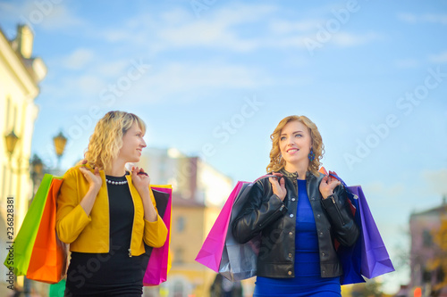 two girls go and smile down the street with shopping bags in their hands