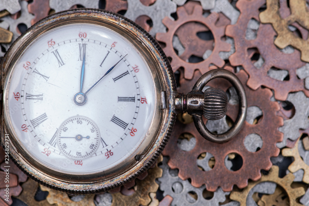 Antique pocket watch and old vintage hour metallic gears on natural stone background.